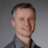 Mann mit freundlichem Lächeln blickt symphatisch in die Kamera