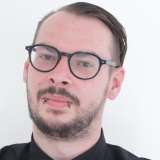 junger Mann, dunkle Haare, Brille, Bart, freundliches lächeln
