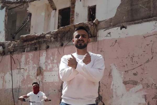 Mann steht mit verschränkten Armen vor Hauswand